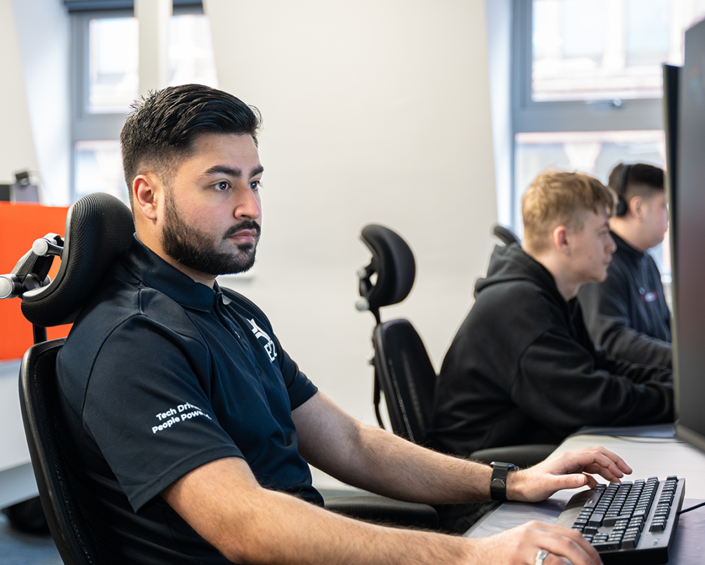 A photo of one of SEP2 analysts working in our 24/7 SOC with two other analysts in the background